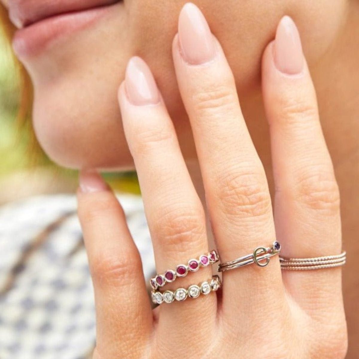 Close-up of a woman's hand wearing multiple stacked rings, including two Bouquet Rings, a Birthstone Ring, a C Letter Ring and Delicate Beaded Bands. 