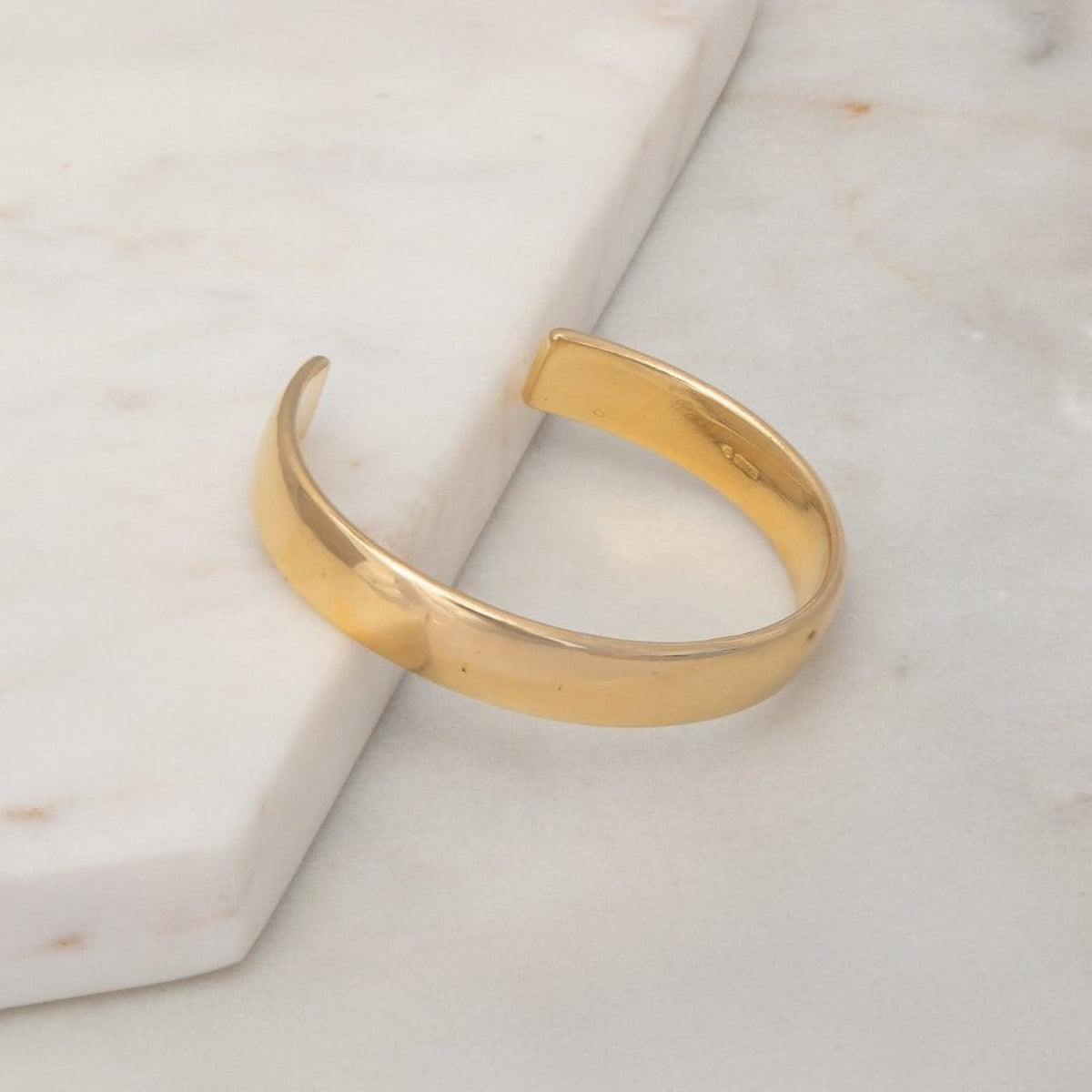 A vermeil gold All in Cuff on a light marble surface.