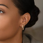 Close-up of woman's ear wearing a White Topaz Chain Earring and a Pave Huggie against a blurred background. 