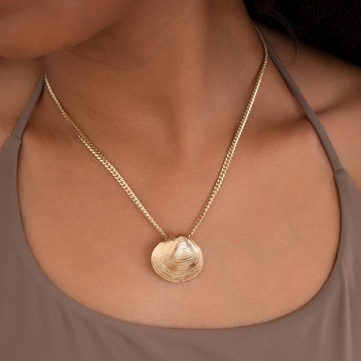 Close-up of a decolletage wearing a yellow gold Chic Cuban Curb Chain with The Golden Venus Shell with a light brown top. 