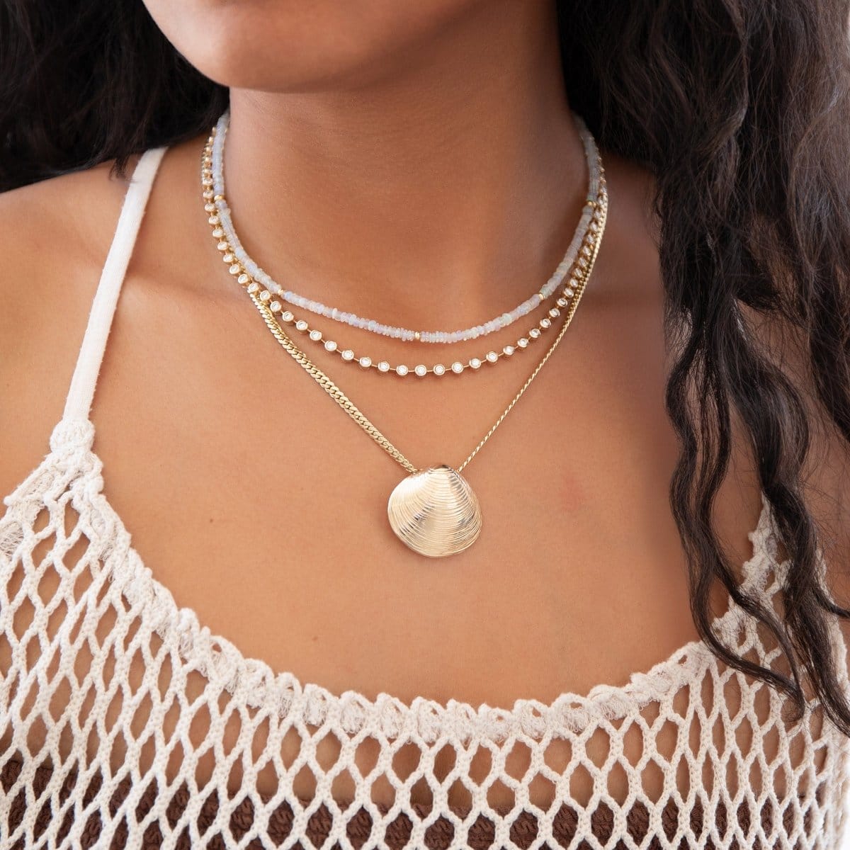 Close-up of a woman's decellotage wearing a Endless Summer Necklace - Pink Sands, The Ultimate Diamond Necklace, Chic Cuban Cuban Chain with The Golden Venus Shell with a cream strap crochet top. 