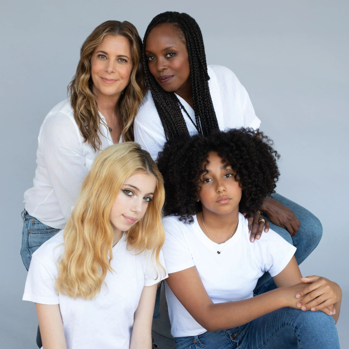 Two women and their daughters all wearing the Enamel Gold Unity Pendant, styled with white tops and blue jeans against a light grey background.