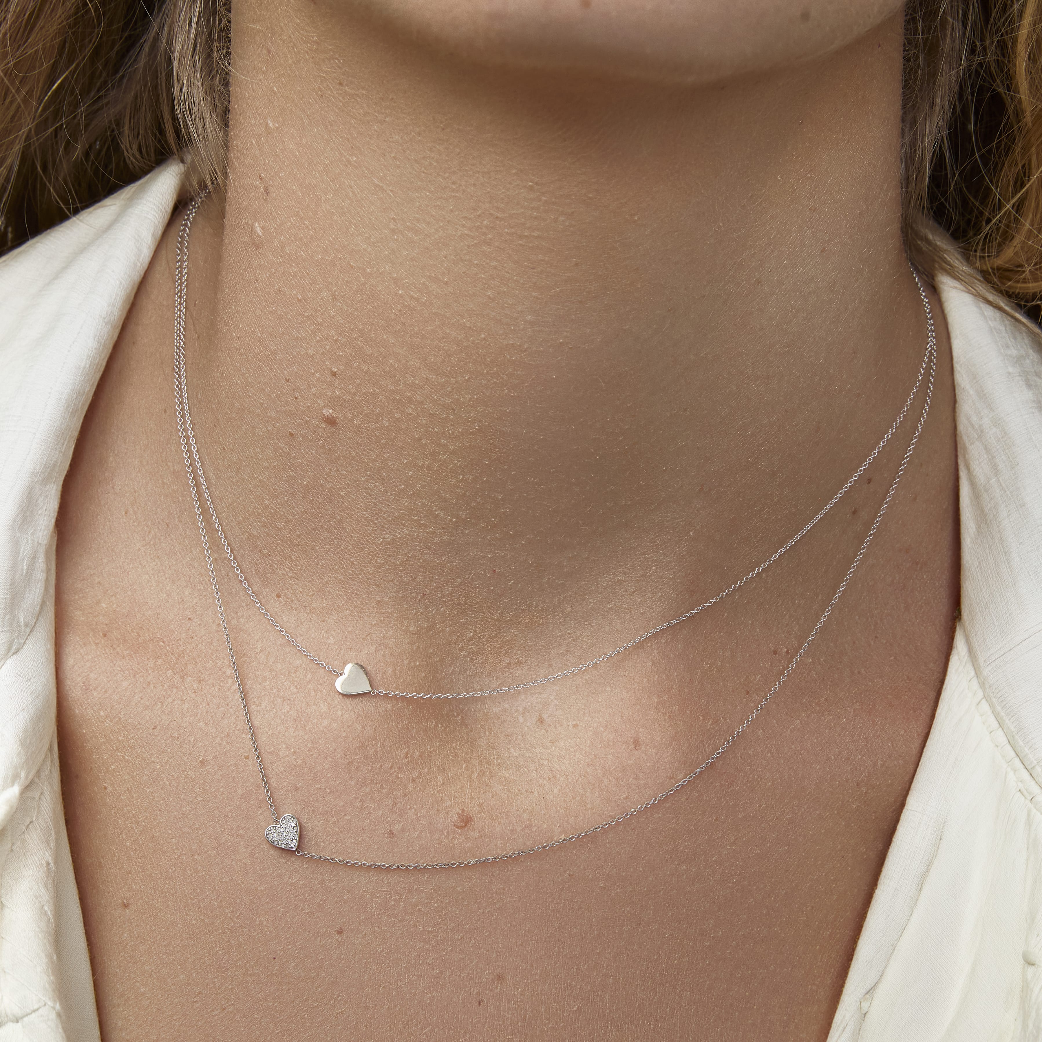 Close-up of a person wearing two silver heart-shaped pendant necklaces.