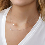 Close-up of a person wearing two silver necklaces with heart pendants on a white background