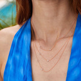 A close-up of a woman’s neck area wearing a blue halter top and three rose gold Monogram Necklaces with Diamond, each with a single letter B, H and C.