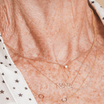 A close-up of a neck wearing a Single Diamond Layering Necklace, a NANA Necklace and a Custom Gold Necklace - 2 Letters, with a white top featuring black stars.