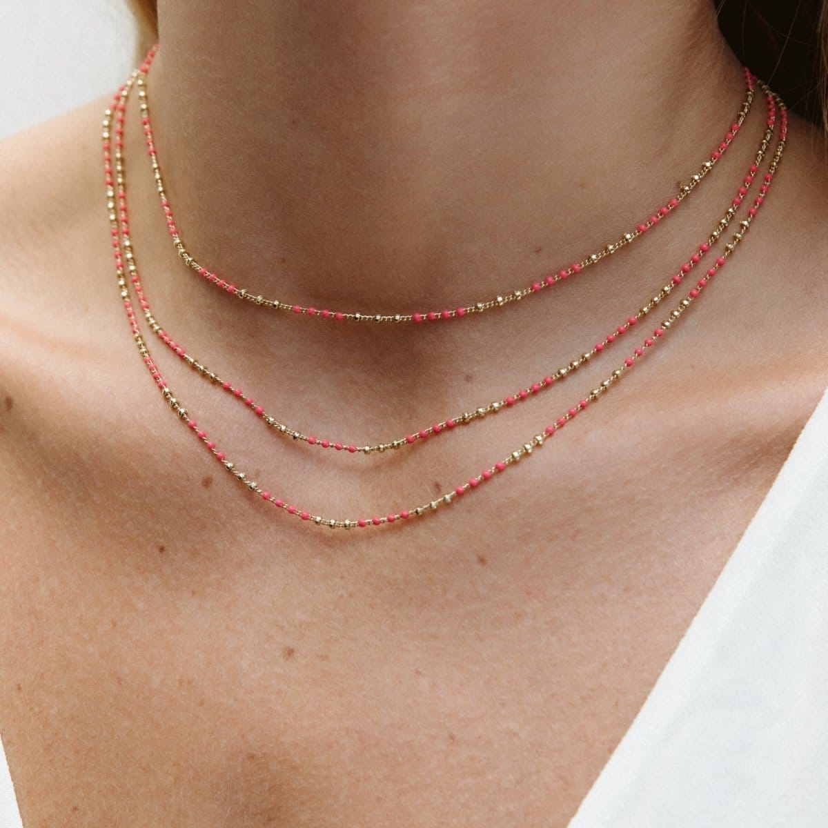 A close-up of a neck wearing three Confetti Necklaces in pink, styled in a white top. 