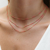 A close-up of a neck wearing three Confetti Necklaces in pink, styled in a white top. 