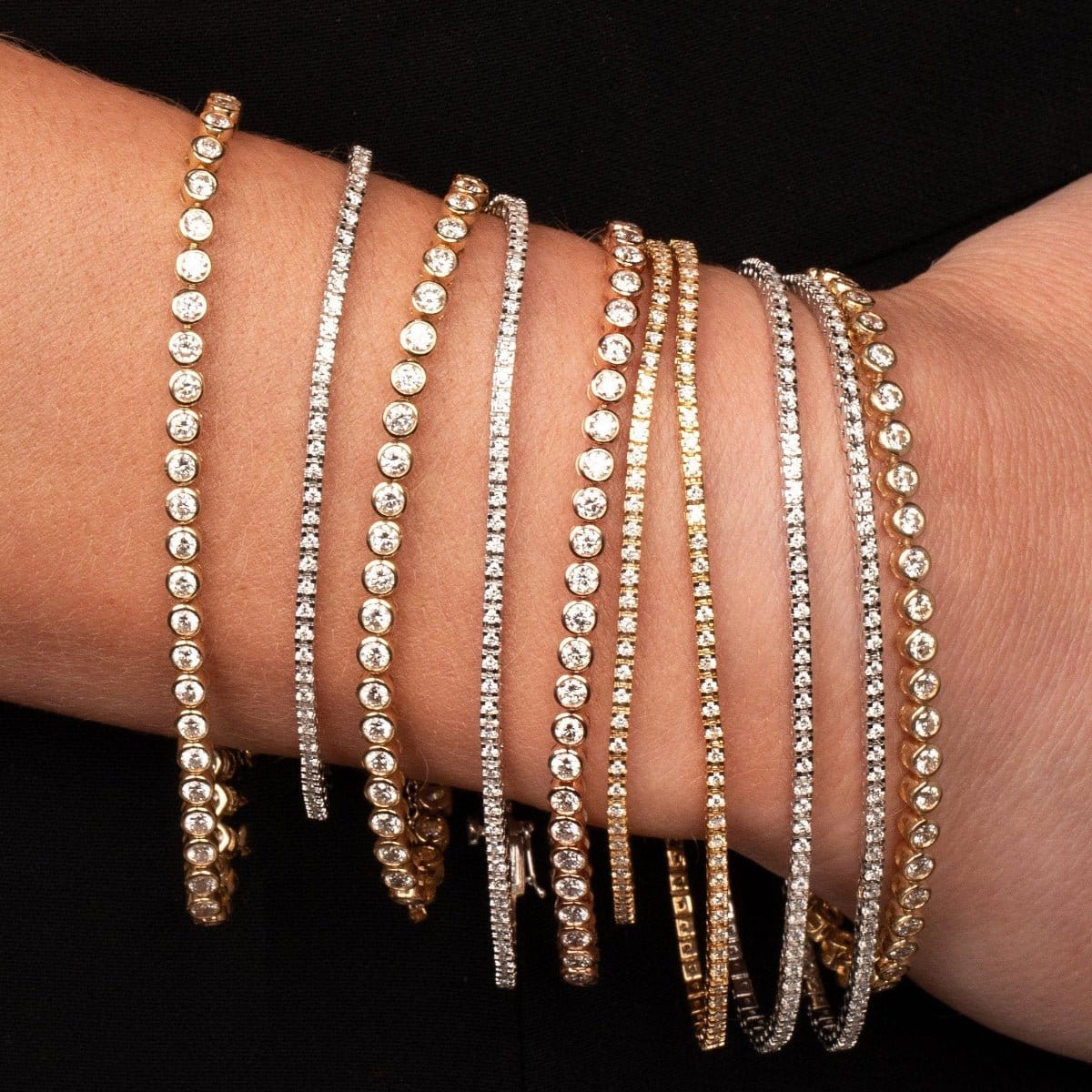 Multiple yellow and white gold Love Set Match Bracelets and Down the Line Bracelets on a wrist against a black background.