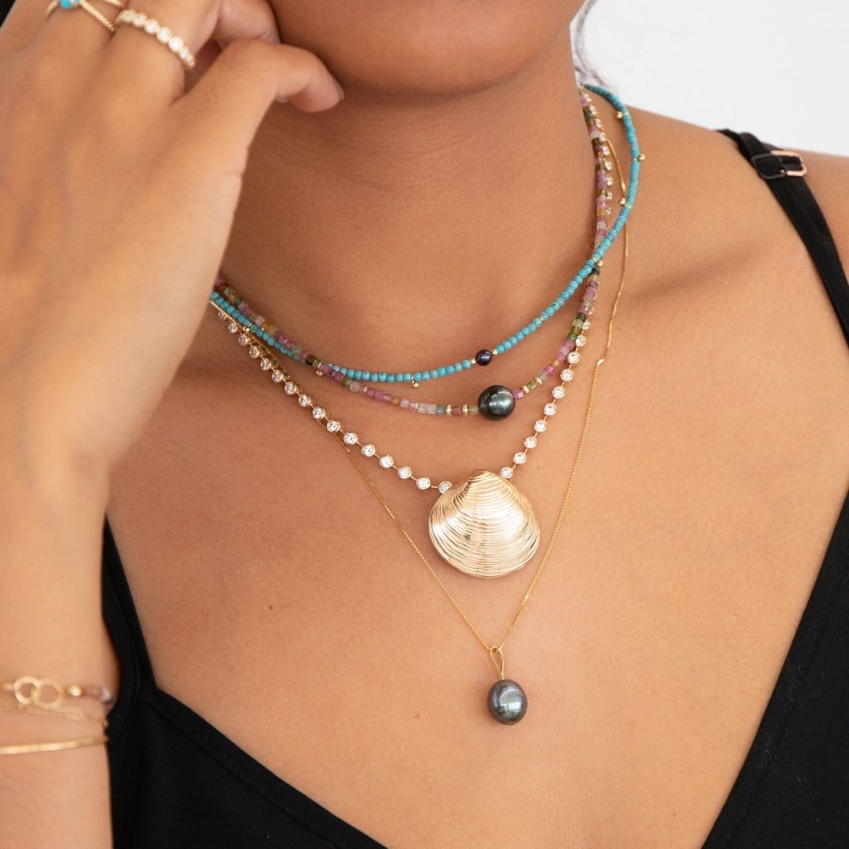 Close-up of a woman's neck wearing Endless Summer Necklaces in Sweet Escape and Santorini, The Ultimate Diamond Necklace with The Golden Venus Shell, Baroque Pearl Necklace and The Evermore Ring, styled in a black strap top. 