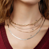 Close-up of a neck wearing a yellow gold Bold Link Chain, a white gold Box Chain, a yellow gold Element Long Link Chain and a white gold Sequence Chain, styled in a deep red top. 