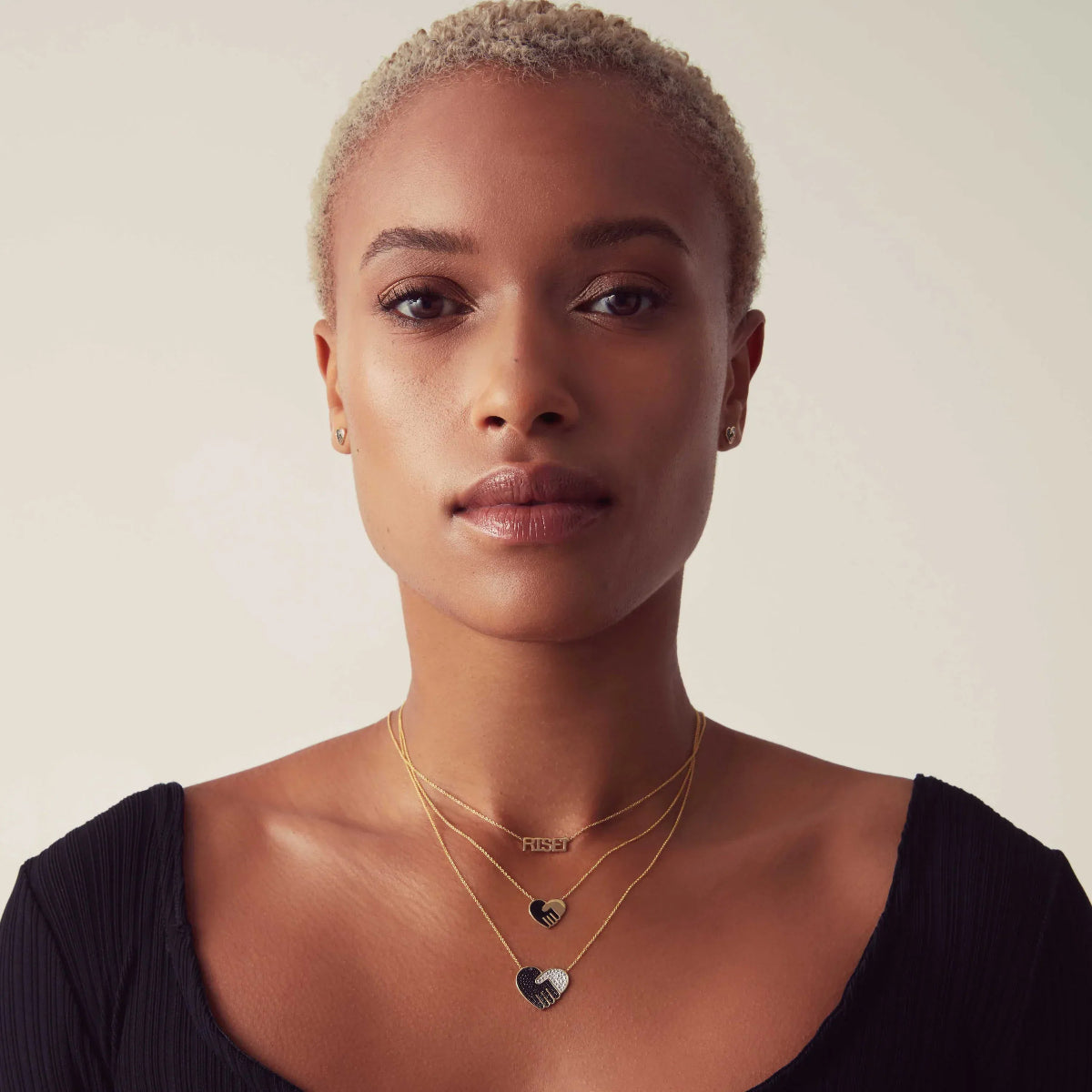 A women wearing Enamel Gold Unity Pendants - Small and Large and a RiseUp Necklace in yellow gold against a light neutral background. 