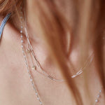 A close-up of a woman's neck wearing three layered necklaces - an Element Short Link Chain, a Monogram Necklace with Heart Yellow Gold and a letter M charm, and a Sage Bouquet Necklace. 