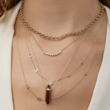 A close-up of a woman's décolletage wearing a Rolo Necklace, a Diamond Arc Layering Necklace, Custom Gold Necklaces - 5 Letters and 3 Letters, and The Courage Retreat Necklace, styled in a white top. 