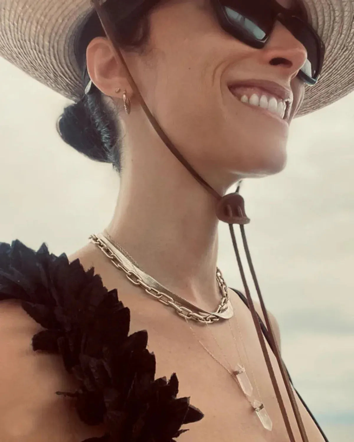 Abigail Spencer wearing a yellow gold Bold Link Chain, Sequence Chain and two Retreat Necklaces in Clarity and Love,  with a straw hat, sunglasses and a black top with a white blurred background. 