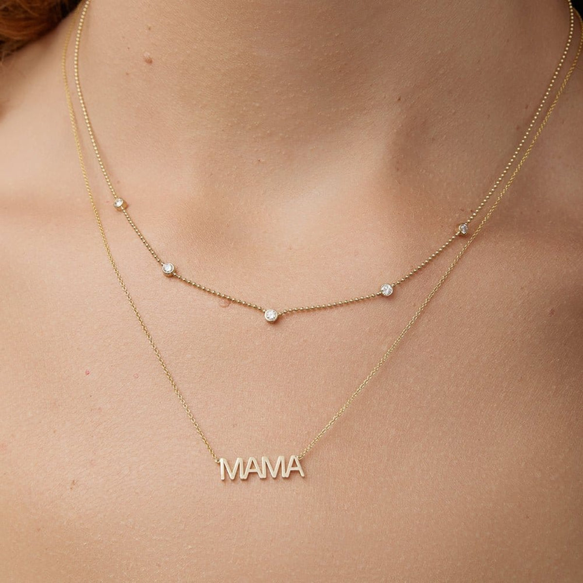 A neck wearing a Quintet Diamond Layering Necklace and a Mama Necklace, both in yellow gold. 