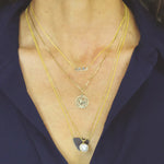 Close-up of a décolletage wearing a MUM Necklace, a Zodiac Necklace - Leo and a Perla Necklace, all in yellow gold, with a navy blue shirt. 