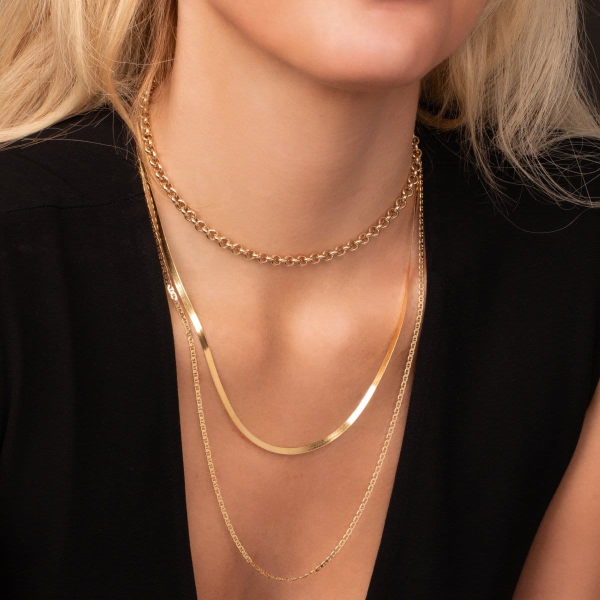 Close-up of a person wearing three gold layering chains.