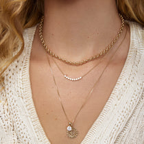 Close-up of a person wearing multiple gold necklaces with a beige sweater.