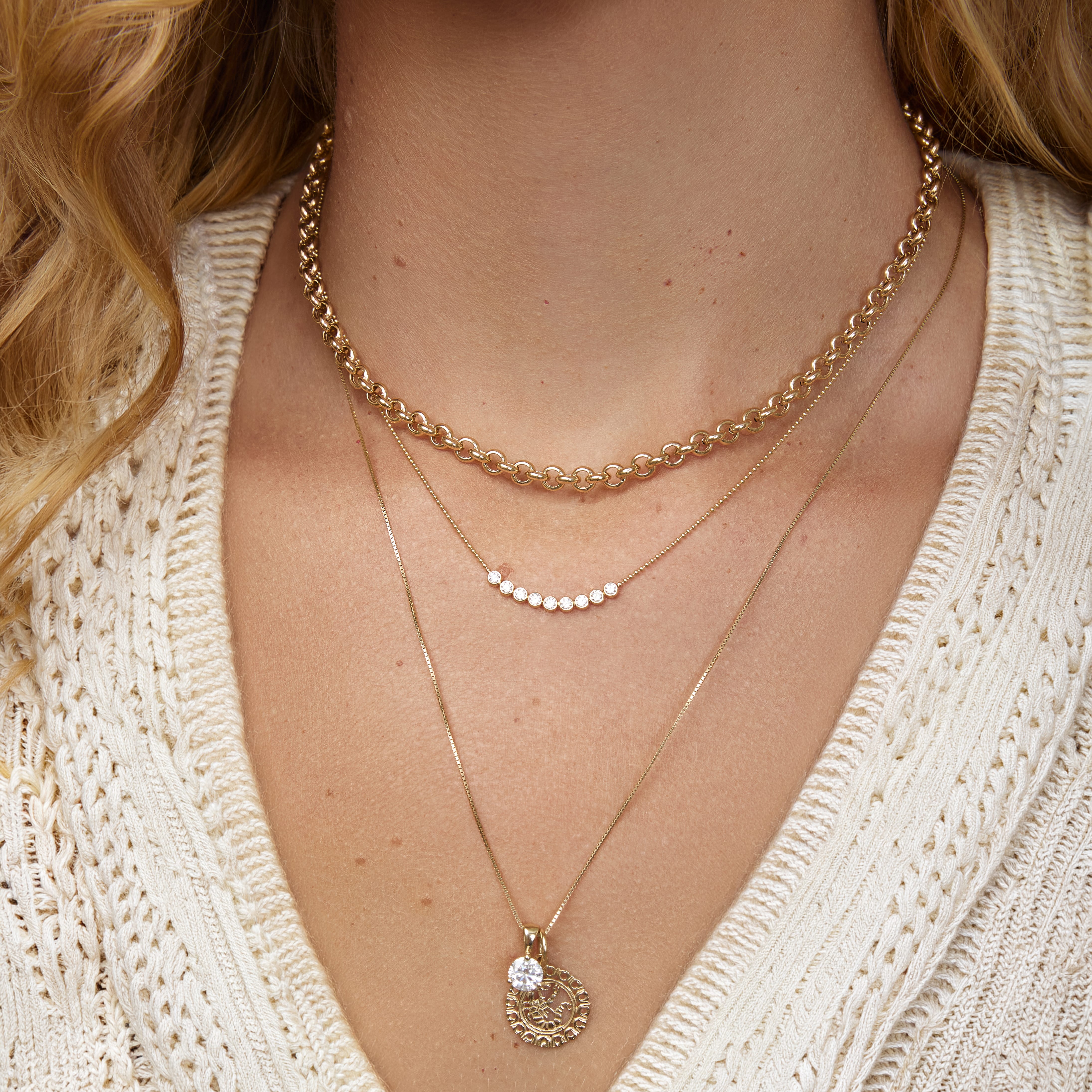 Close-up of a person wearing multiple gold necklaces with a beige sweater.