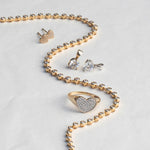 The Ultimate Diamond Necklace, a Love on the Rocks Ring, Pave Charm Studs -  Heart and two Diamond Pendants laid on top of a light grey surface. 