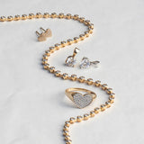 The Ultimate Diamond Necklace, a Love on the Rocks Ring, Pave Charm Studs -  Heart and two Diamond Pendants laid on top of a light grey surface. 