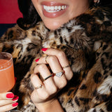 Close-up of a woman wearing two Birthstone Rings, a Geo Stacking Ring, a Love on the Rocks Ring and a Link Ring, all in yellow gold, styled with a leopard fur jacket while holding a cocktail.