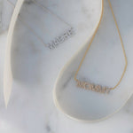 A Pavé Madre Necklace in white gold and a Pavé MOMMY Necklace in yellow gold on a white marble background. 
