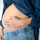 Pregnant person wearing a blue shirt and jeans, holding their belly.