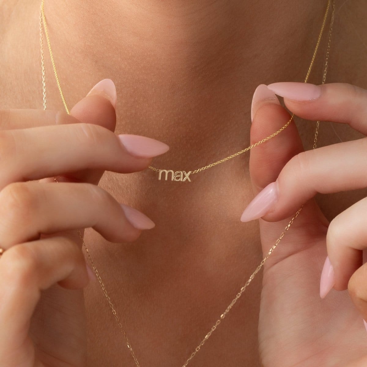 small lowercase nameplate necklace 'max' in yellow gold being held in hand as a lifestyle image.