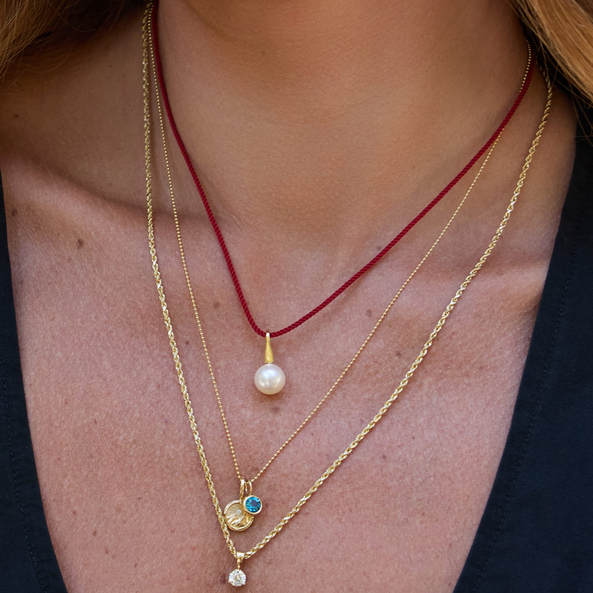 Close-up of a person wearing multiple gold necklaces with pendants on a plain background