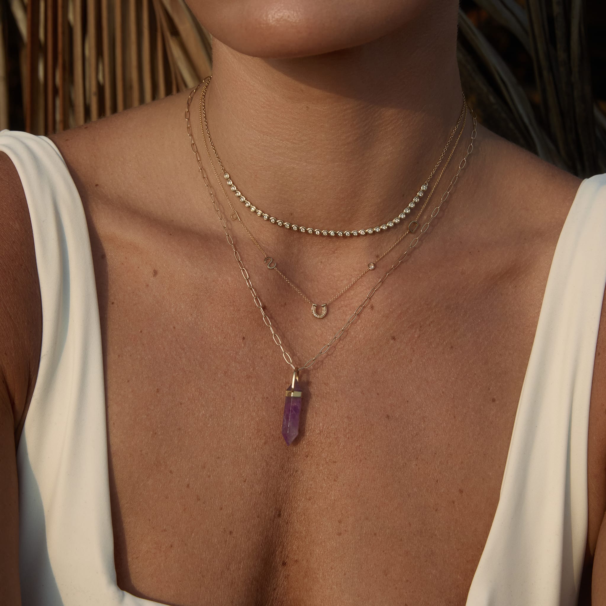 Close-up of a person wearing gold necklaces with a purple pendant.