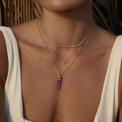 Close-up of a person wearing gold necklaces with a purple pendant.