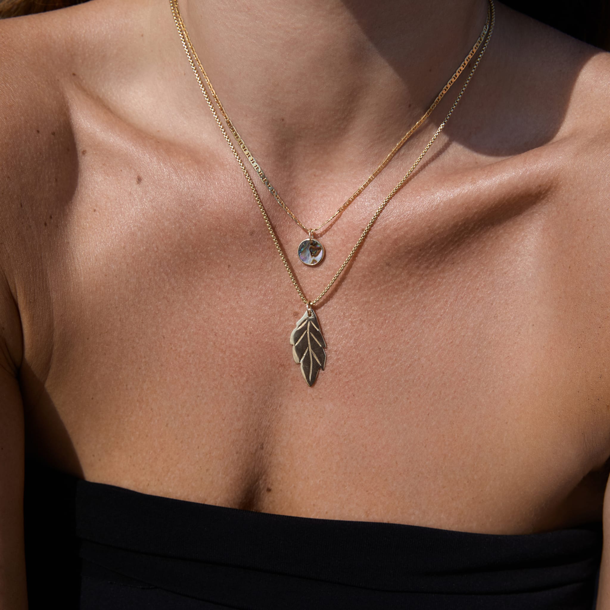 Model wearing the Box Chain with a leaf pendant, layered with an Abalone Pendant necklace.
