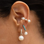 Close-up of Maya Brenner Orbit Pearl Ear Cuff worn in an ear stack with turquoise huggie hoops and pearl earring charms, no piercing ear cuff