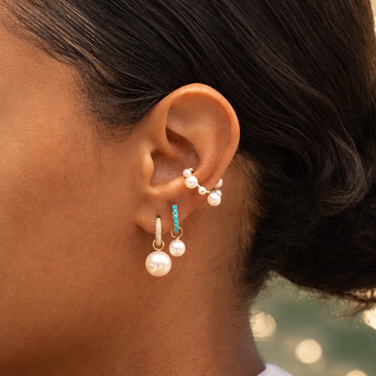 Model wearing Maya Brenner Orbit Pearl Ear Cuff styled with turquoise huggie hoops and pearl earring charms in a layered ear stack