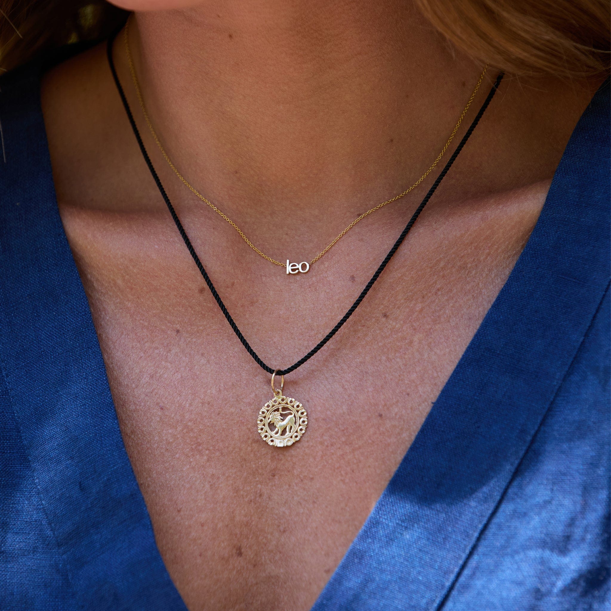 Close-up of a person wearing two necklaces with a blue garment in the background