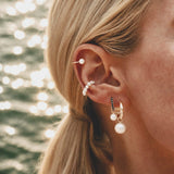 Model wearing Maya Brenner Solitaire Pearl Ear Cuff styled in a layered ear stack with pearl halo ear cuff, black diamond huggie hoops, and pearl earring charms