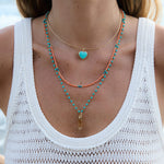 Close-up of a person wearing layered necklaces with a white sleeveless top.