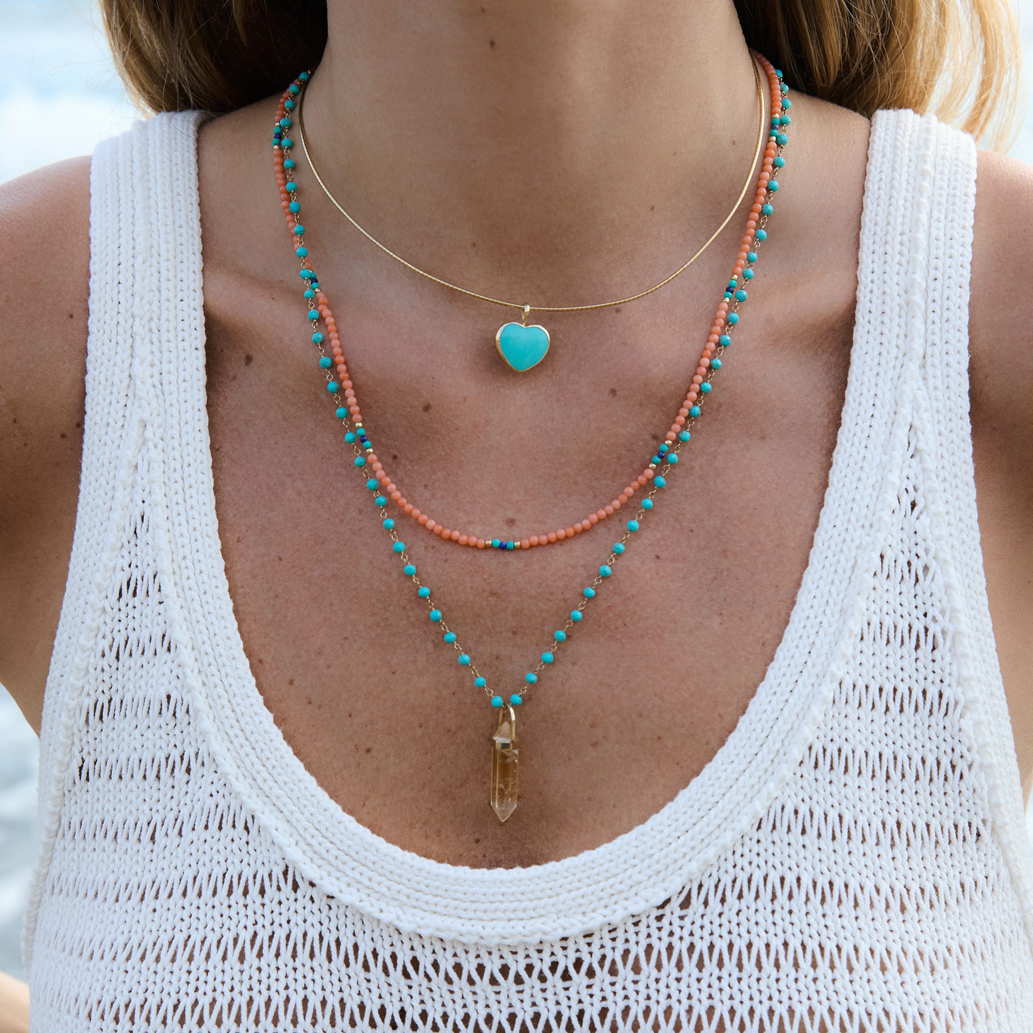 Close-up of a person wearing layered necklaces with a white sleeveless top.