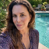 Maya Brenner wearing a freshwater pearl earring charm styled on a gold hoop, paired with layered delicate gold necklaces, in an outdoor setting.