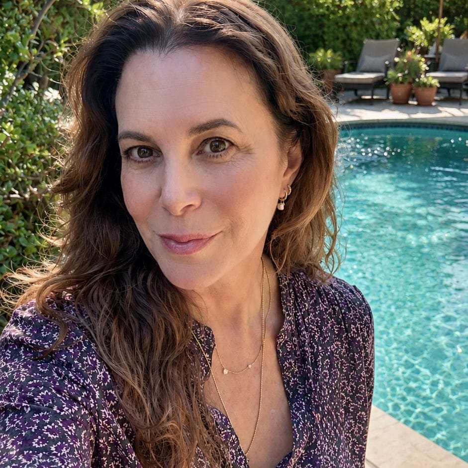 Maya Brenner wearing a freshwater pearl earring charm styled on a gold hoop, paired with layered delicate gold necklaces, in an outdoor setting.