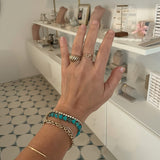 Hand wearing multiple gold and turquoise bracelets with a blurred indoor background