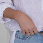 Close-up of a woman’s arm wearing a Mini Bubble Bracelet, two Delicate Beaded Bands and a Twinkle Twinkle Ring, with a white shirt and light blue jeans.