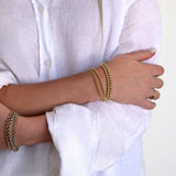 Close-up of arms wearing mixed metal jewellery - a Luxe Bubble Bracelet Set, Rolo Bracelets, Diamond Cut Bracelets, Delicate Beaded Bands and a Twinkle Twinkle Ring, with the person’s white shirt in the background.