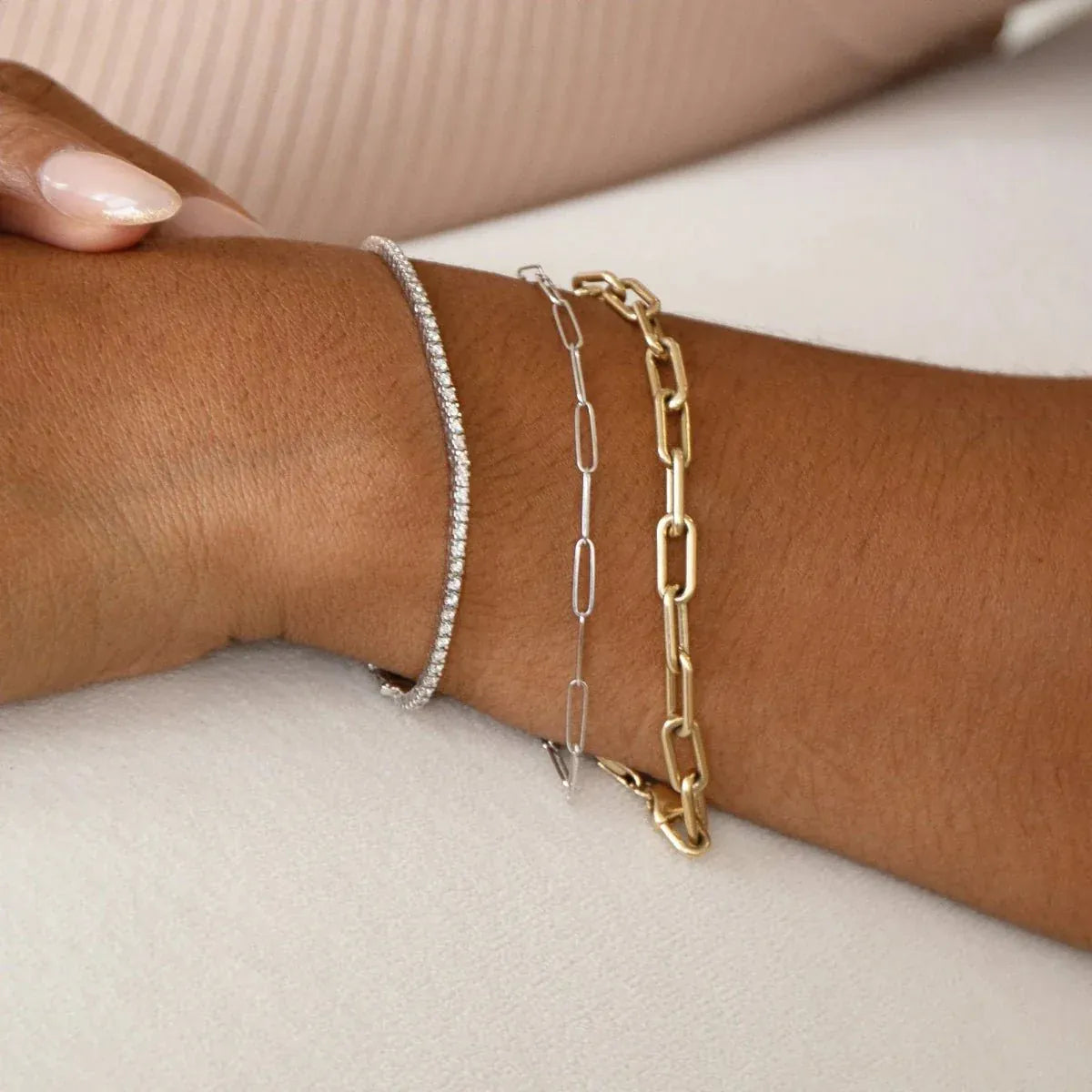 A close-up of a wrist wearing a white gold Down the Line Bracelet, a white gold Element Long Link Bracelet and a yellow gold Bold Link Bracelet. 