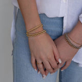Close-up of hands wearing mixed metal jewellery - a Luxe Bubble Bracelet Set, Rolo Bracelets, Diamond Cut Bracelets, Delicate Beaded Bands and a Twinkle Twinkle Ring, with jeans and a white shirt in the background.