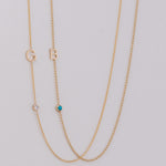 Two delicate gold chain necklaces laid flat on a light gray background. One necklace features a gold letter 'G' and a small clear stone, while the other features a gold letter 'B' and a small turquoise blue stone.