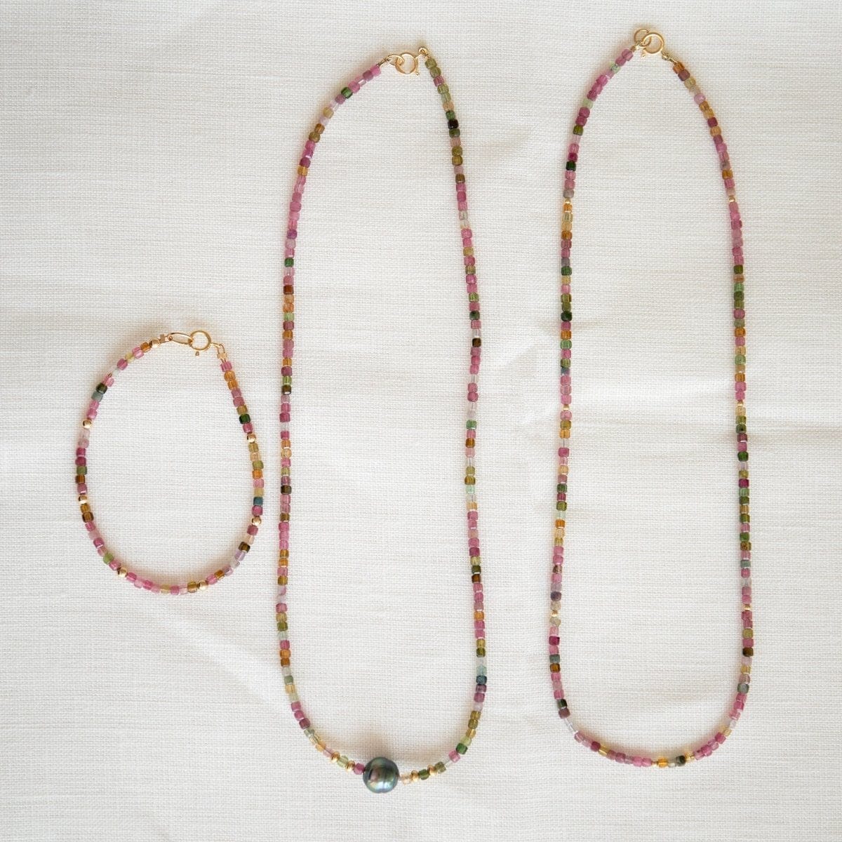 Endless Summer Necklaces in Coral Reef and Sweet Escape and an Endless Summer Bracelet in Coral Reef on a cream fabric background.