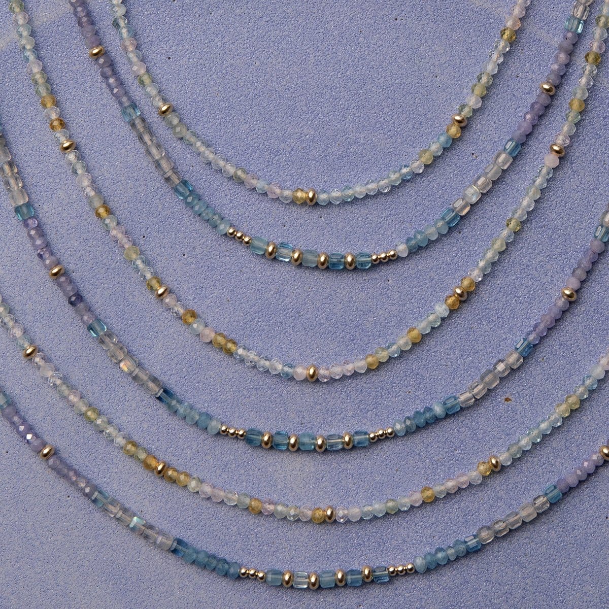 Several Endless Summer Necklaces in Saint-Tropez and Blue Lagoon, laid against a purple background. 